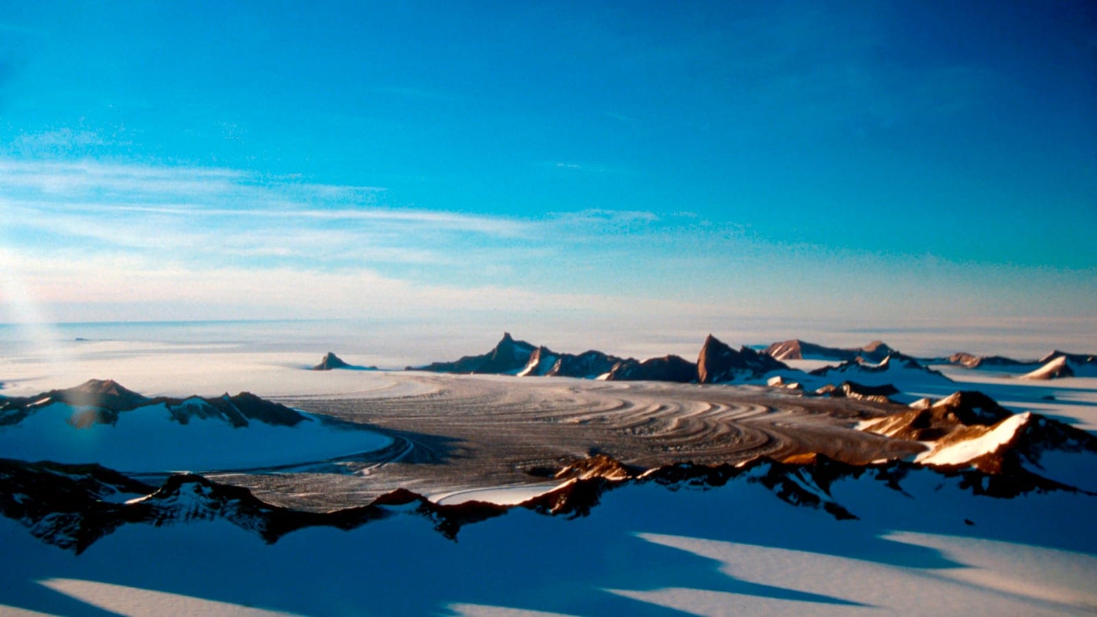 View northwest over the Schussel Cirque, a glaciated valley among the dark rock nunataks of the Wohlthat Mountains in central Dronning Maud Land, East Antarctica.