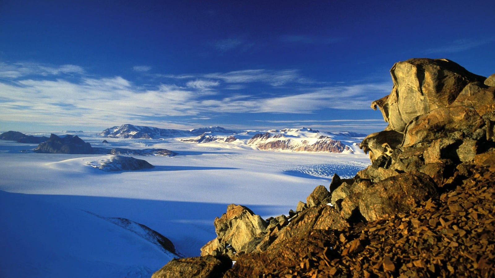 Sunlit rock scree above an ice sheet and dark nunataks in the Transantarctic Mountains, Antarctica.