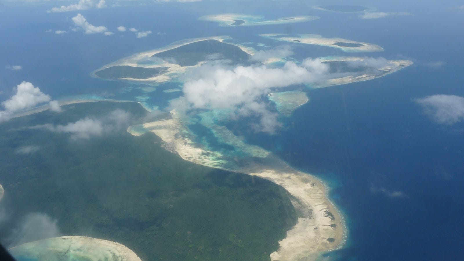 Aerial view of forested Tayando Islands and shallow tropical reefs in Indonesia.