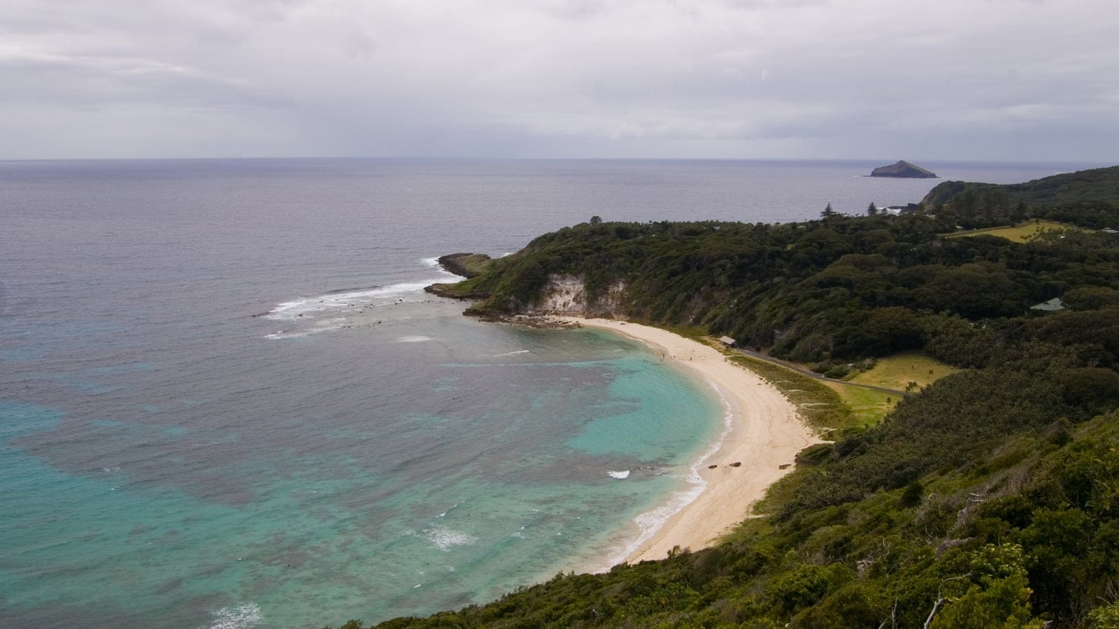 Curving sand beach and reef lagoon below forested slopes and cleared paddocks, Lord Howe Island.