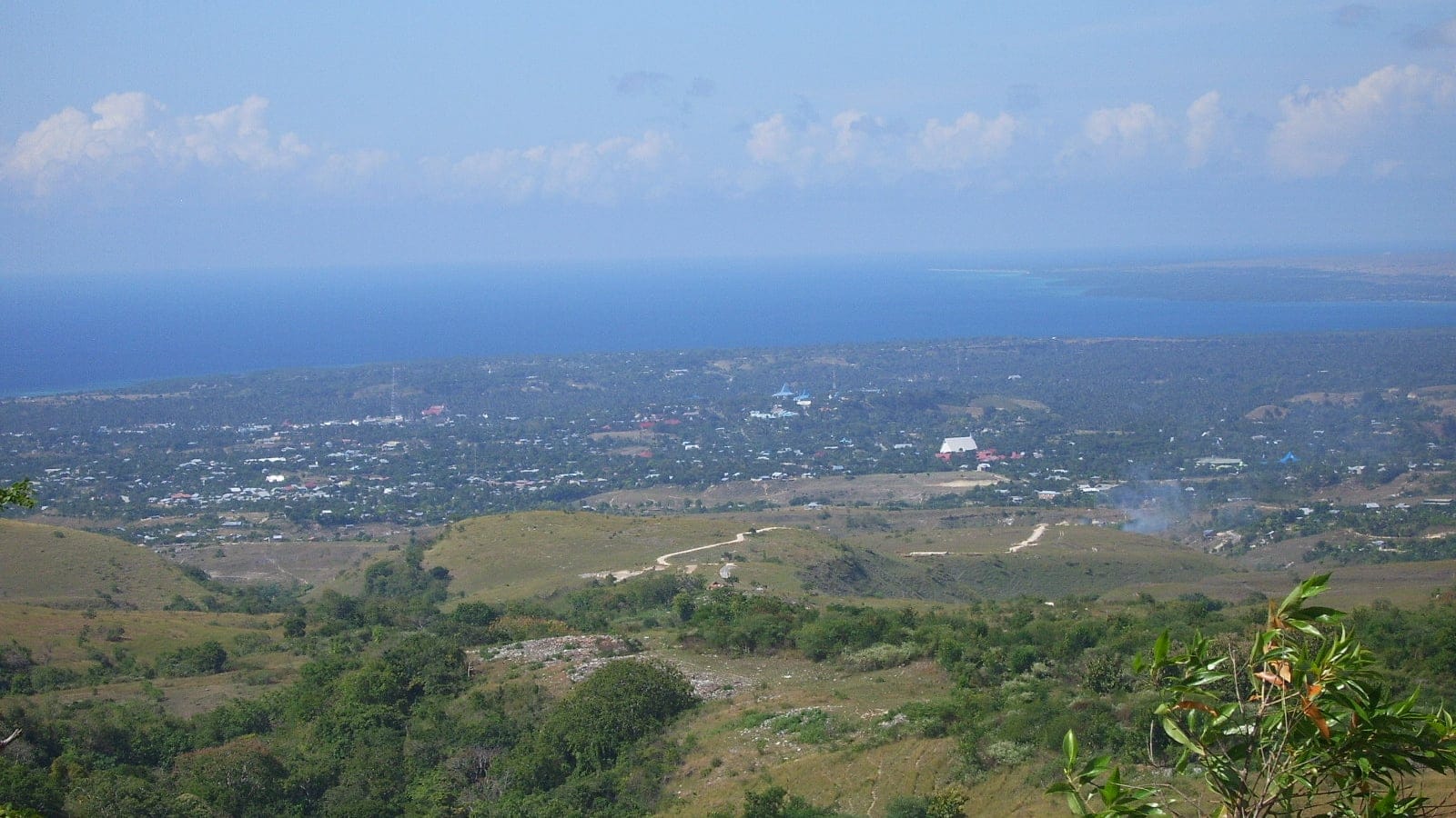Colinas cubiertas de hierba y matorral disperso sobre la ciudad de Waingapu y el mar, Sumba, Indonesia.