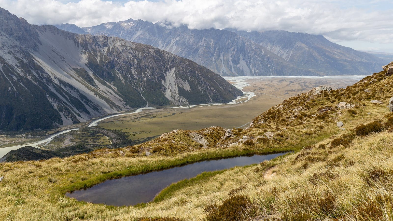 Tussock grassland and a small tarn above a braided glacial valley at Sealy Tarns, Aoraki / Mount Cook National Park, New Zealand.