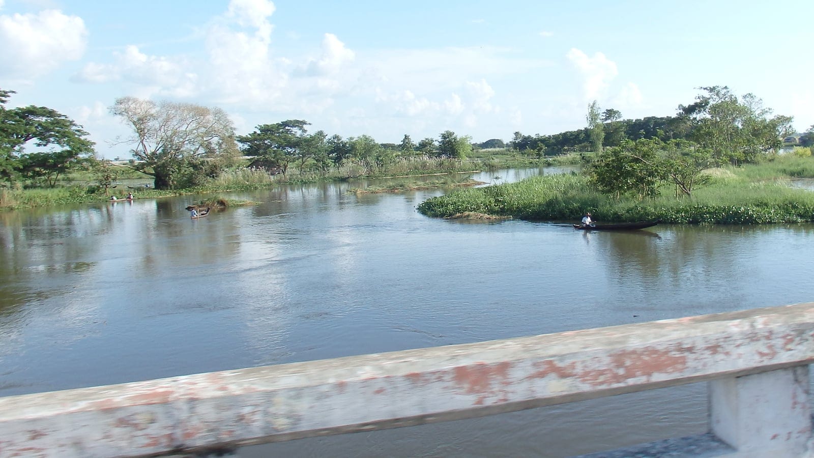 Water hyacinth mats and dugout canoes on a river channel seen from a bridge near Maubin, Myanmar.