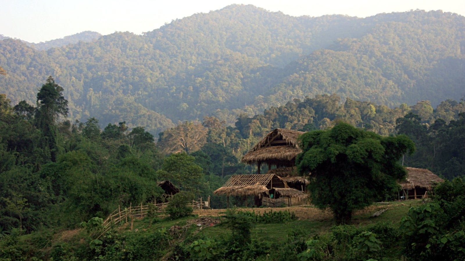 Thatched huts in a clearing below forested hills in Pu Mat National Park, Vietnam.