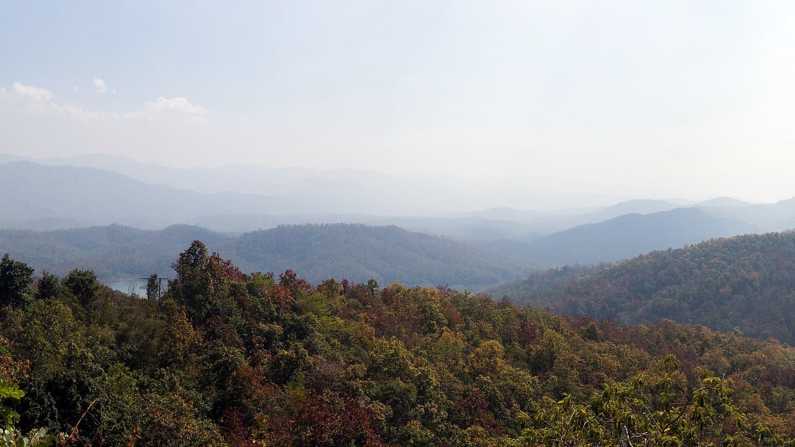 Amplia panorámica en la estación seca sobre las estribaciones boscosas de la cordillera Phi Pan Nam, por encima del embalse de la presa Sirikit, con árboles caducifolios que se tornan pardos al perder las hojas para el largo periodo seco.