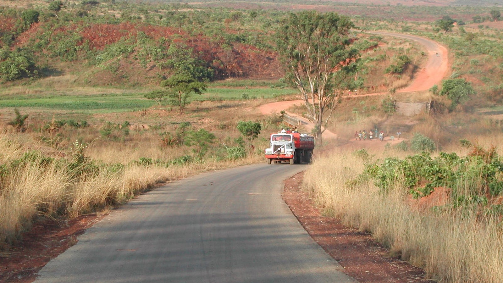Sealed road and a laden truck crossing dry grass and red lateritic slopes near Huambo, Angola.