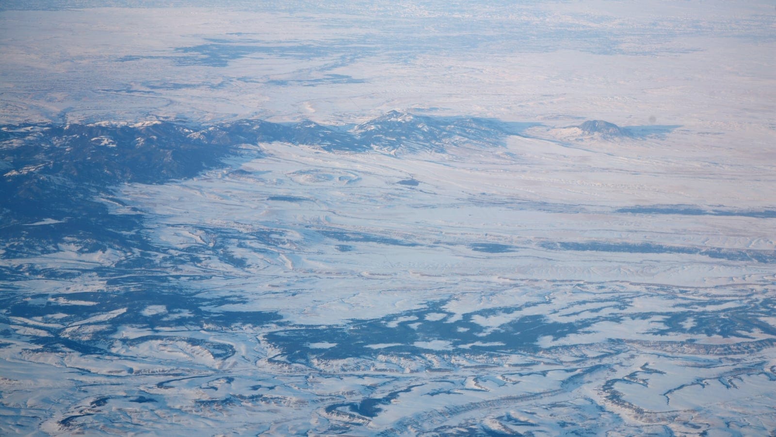 Snow-blanketed valley floor and dark forested ridges of the Judith Mountains from the air, Montana.