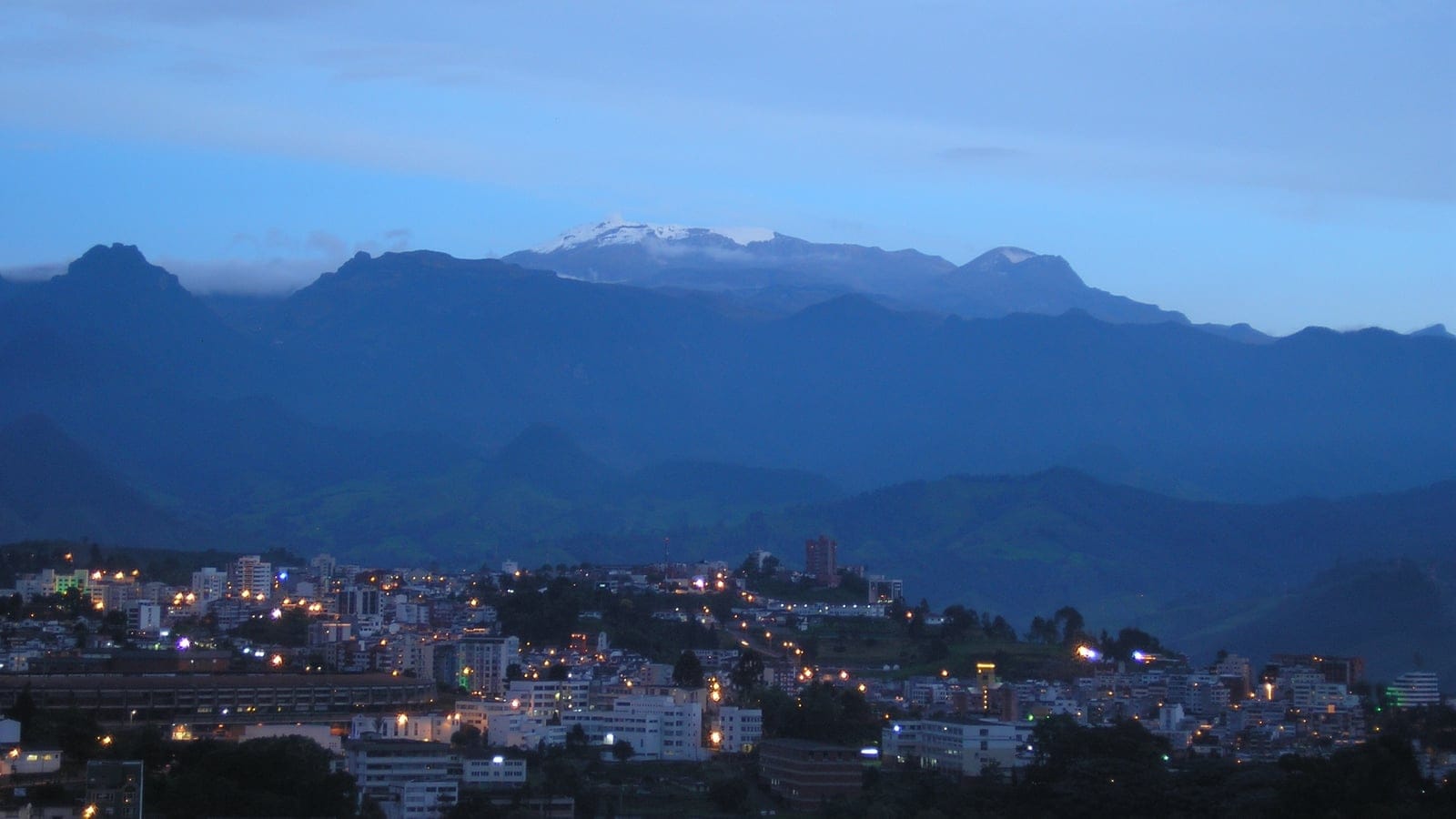Lights of Manizales below dark ridges and the snow cap of Nevado del Ruiz at dusk, Colombia.