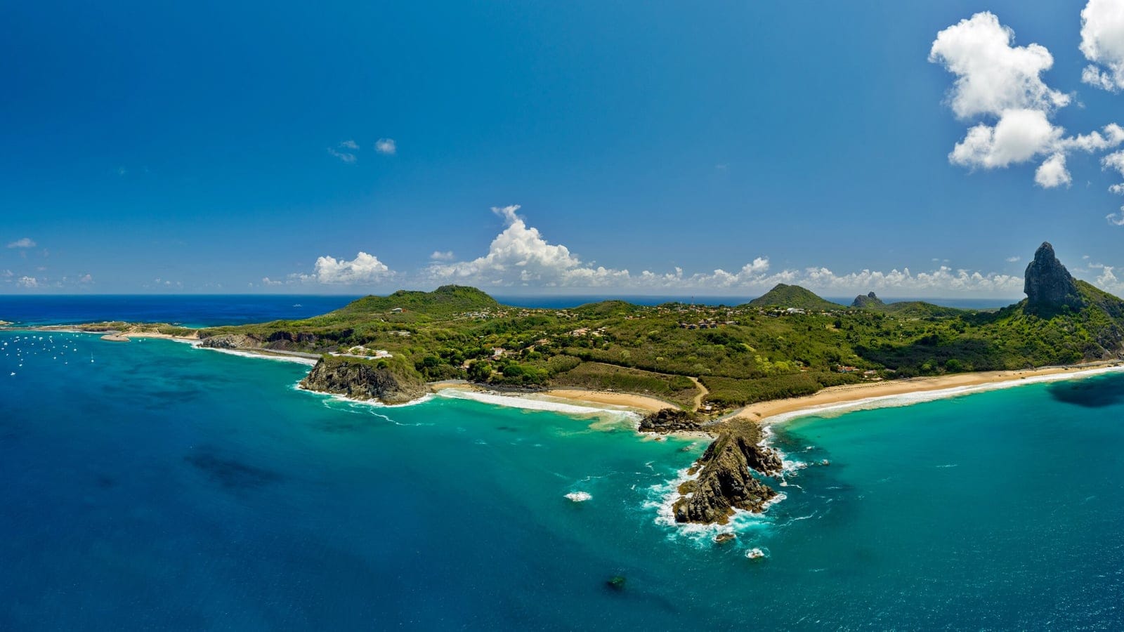 Aerial panorama of Fernando de Noronha with the Morro do Pico spire above scrubby hills and reef fringed beaches, Brazil.