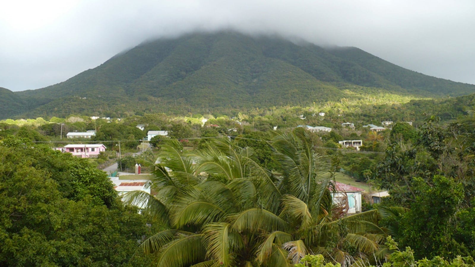 Cloud capping the forested cone of Nevis Peak above coconut palms and scattered village roofs, Nevis.