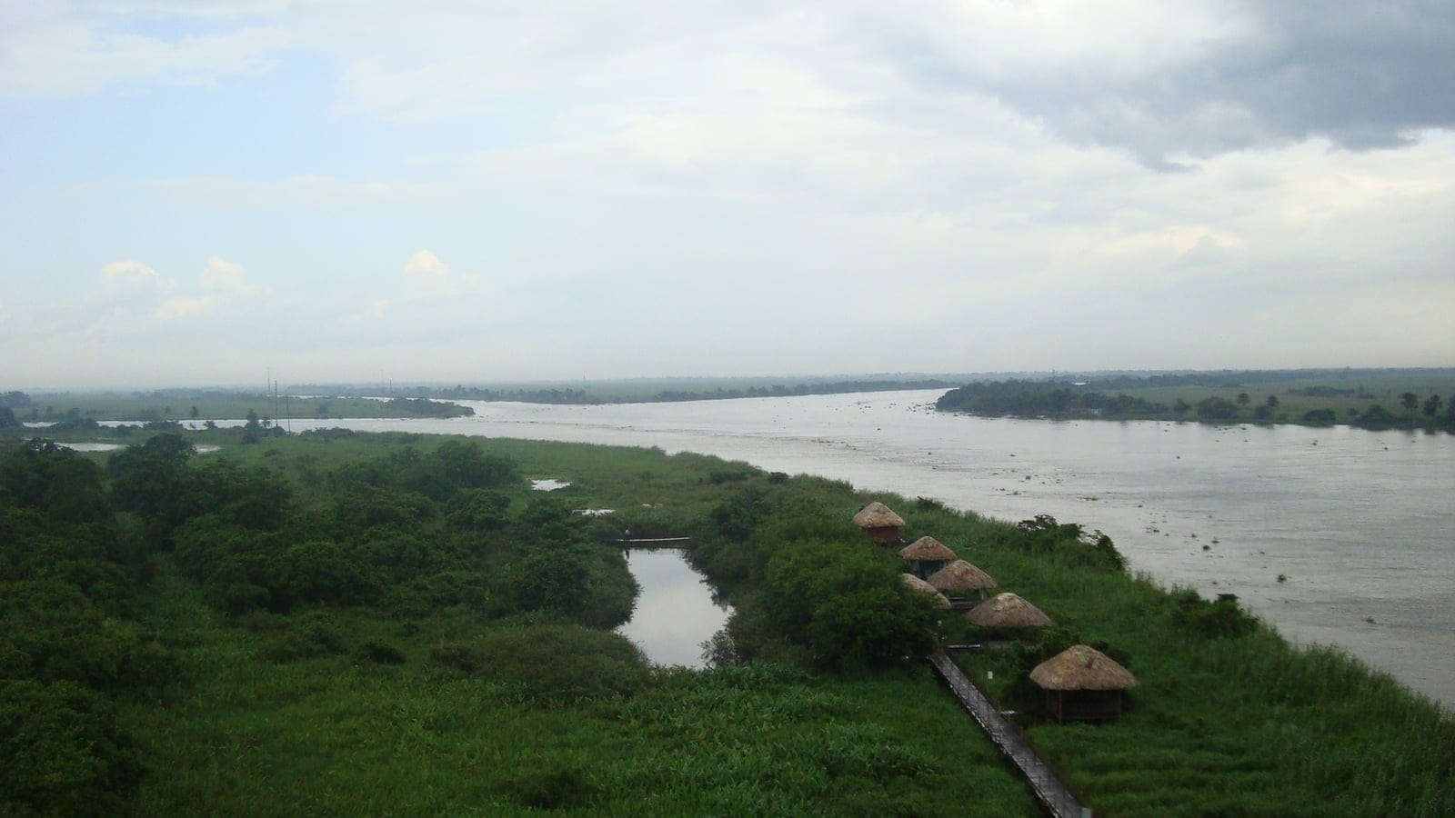 Thatched shelters on a grassy bank above a wide river channel, Pantanos de Centla, Tabasco, Mexico.