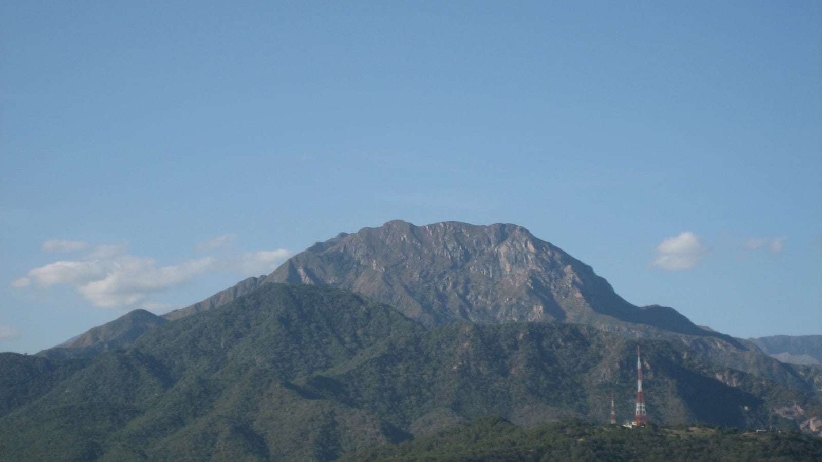 Forested slopes below the bare rock crest of Cerro Murillo, with radio masts on a spur, Sierra Nevada de Santa Marta, Colombia.