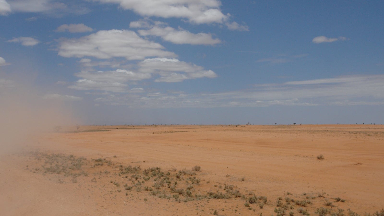 Expansive flat arid desert plain of the Chalbi Desert in northern Kenya, pale sandy ground under an open sky with sparse low vegetation.