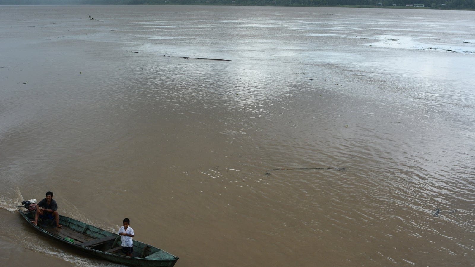 Silt-brown Amazon water with a motorised dugout canoe and a thin forest line on the far bank, Peru.