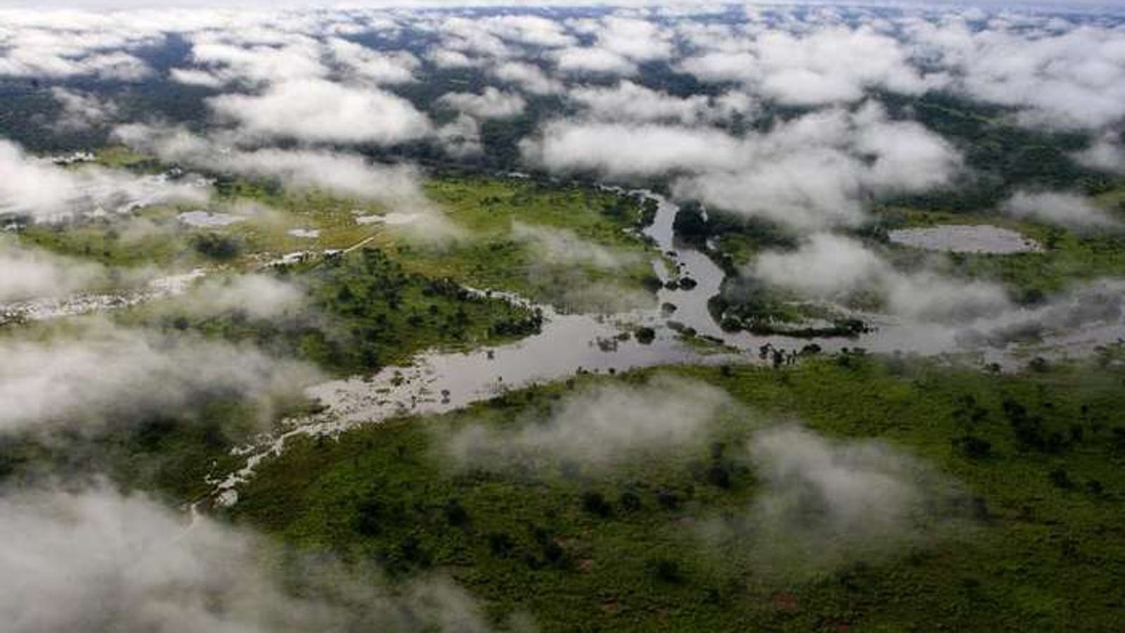 Canais fluviais serpenteando pela savana arborizada vistos através de nuvens esparsas sobre o Parque Nacional de Garamba, República Democrática do Congo.