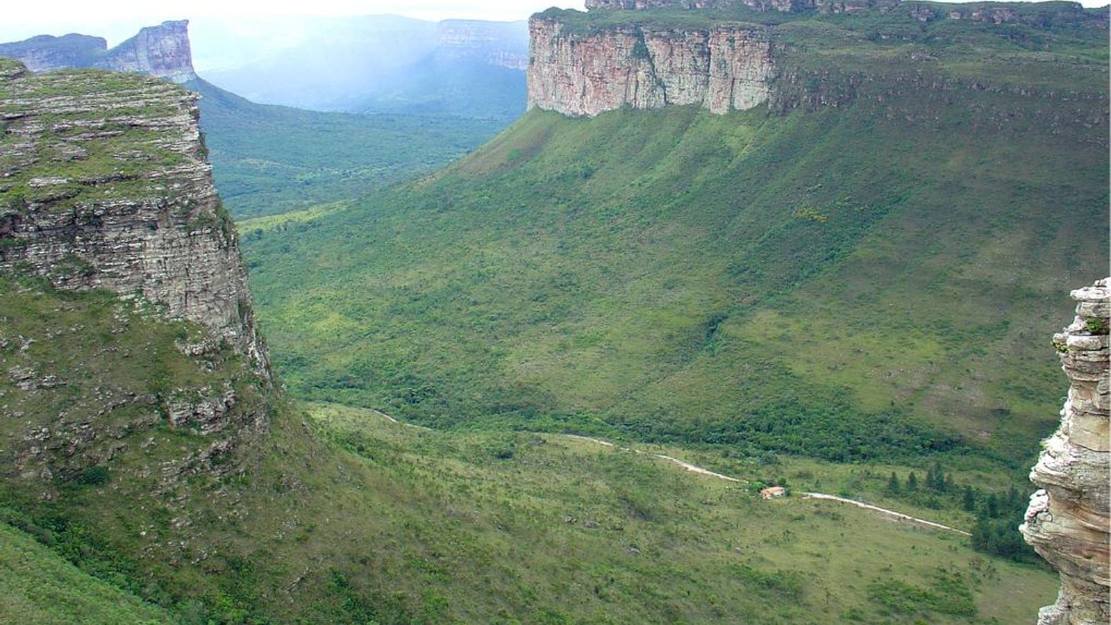 Sandstone table mountains above grassy slopes and dark valley woodland, Chapada Diamantina, Bahia, Brazil.