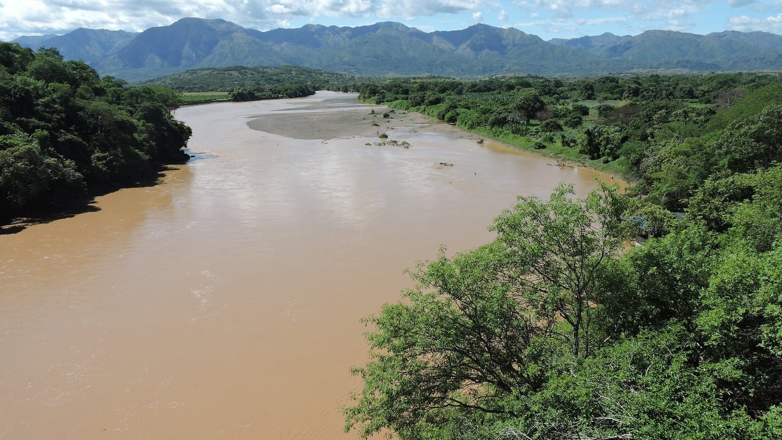 Silt-laden Magdalena River between wooded banks below Andean foothills near Villavieja, Huila, Colombia.