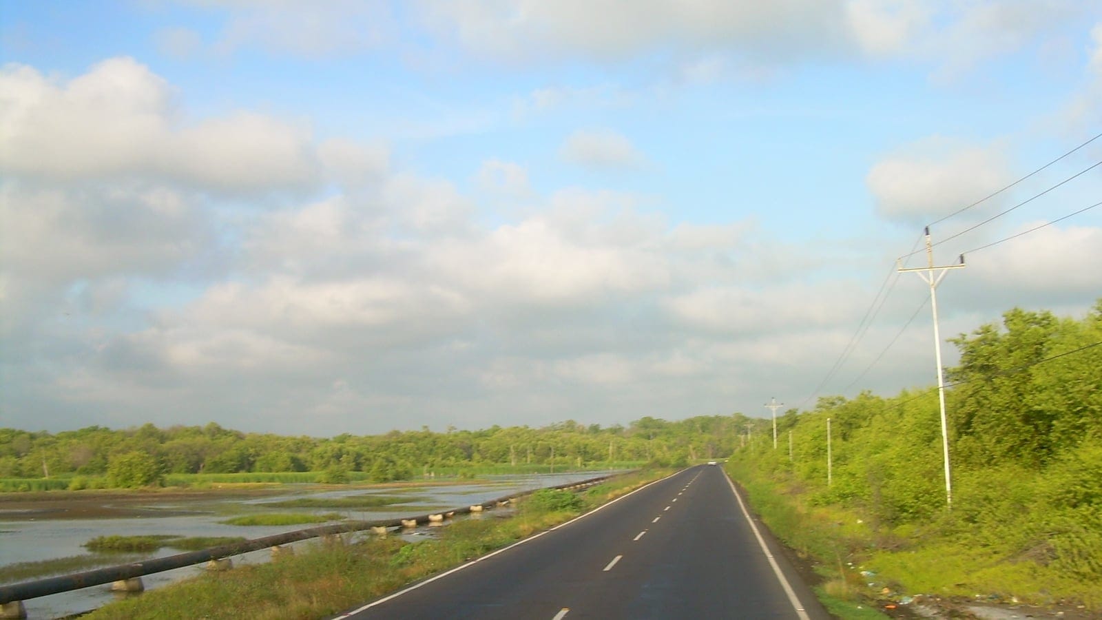 Paved highway and a pipeline beside a shallow lagoon backed by low green scrub near Sinamaica, Zulia, Venezuela.