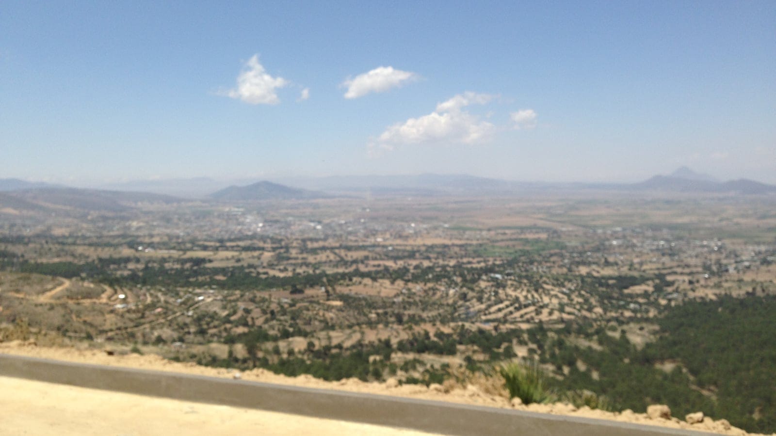 Hazy farmed plain seen over a concrete roadside barrier on the Llanura de Libres, Puebla, Mexico.