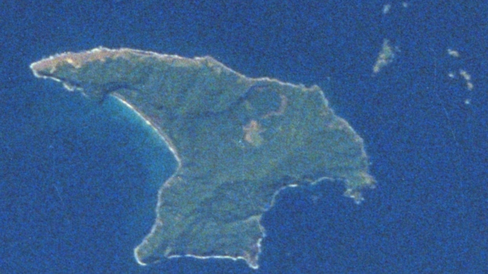 Satellite view of dark forest cover and surf-fringed cliffs on Raoul Island, Kermadec Islands, New Zealand.