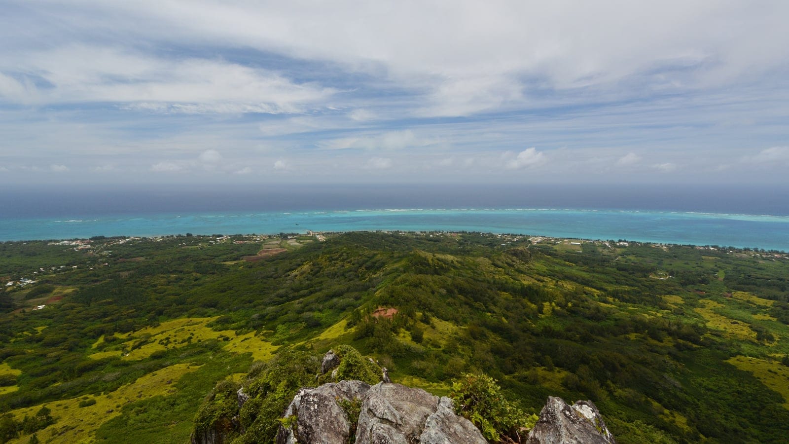 Scrub and fern covered ridge dropping to a settled coastal plain and reef lagoon, Tubuai, Austral Islands.