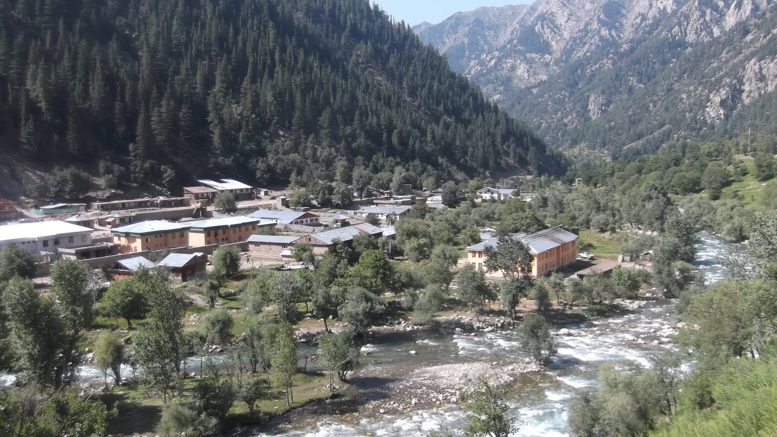 A village beside a boulder braided river below conifer clad slopes at Parun, Nuristan, Afghanistan.