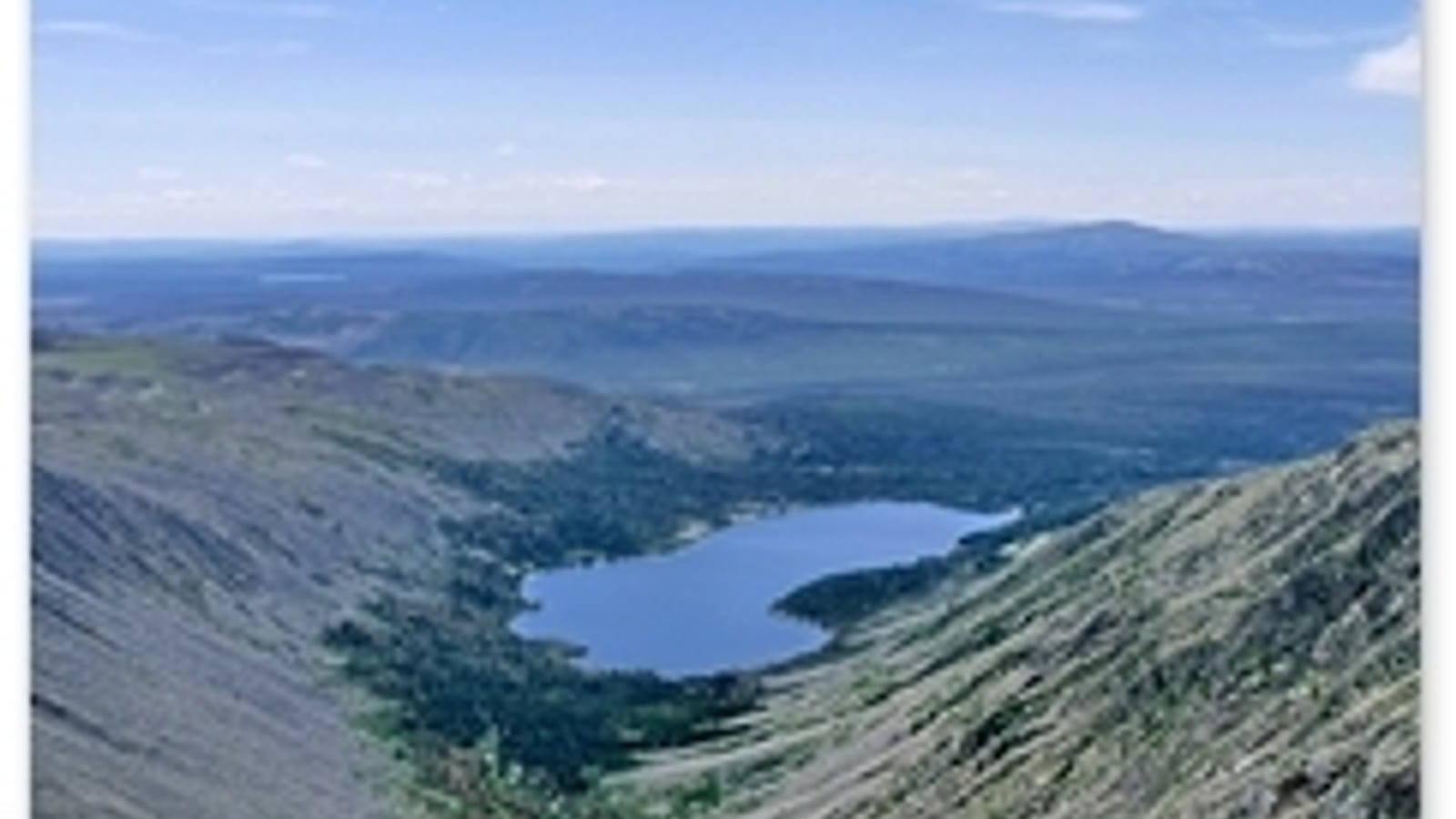 Bare scree slope above distant taiga and a valley lake, Sokhondo Nature Reserve, Russia.