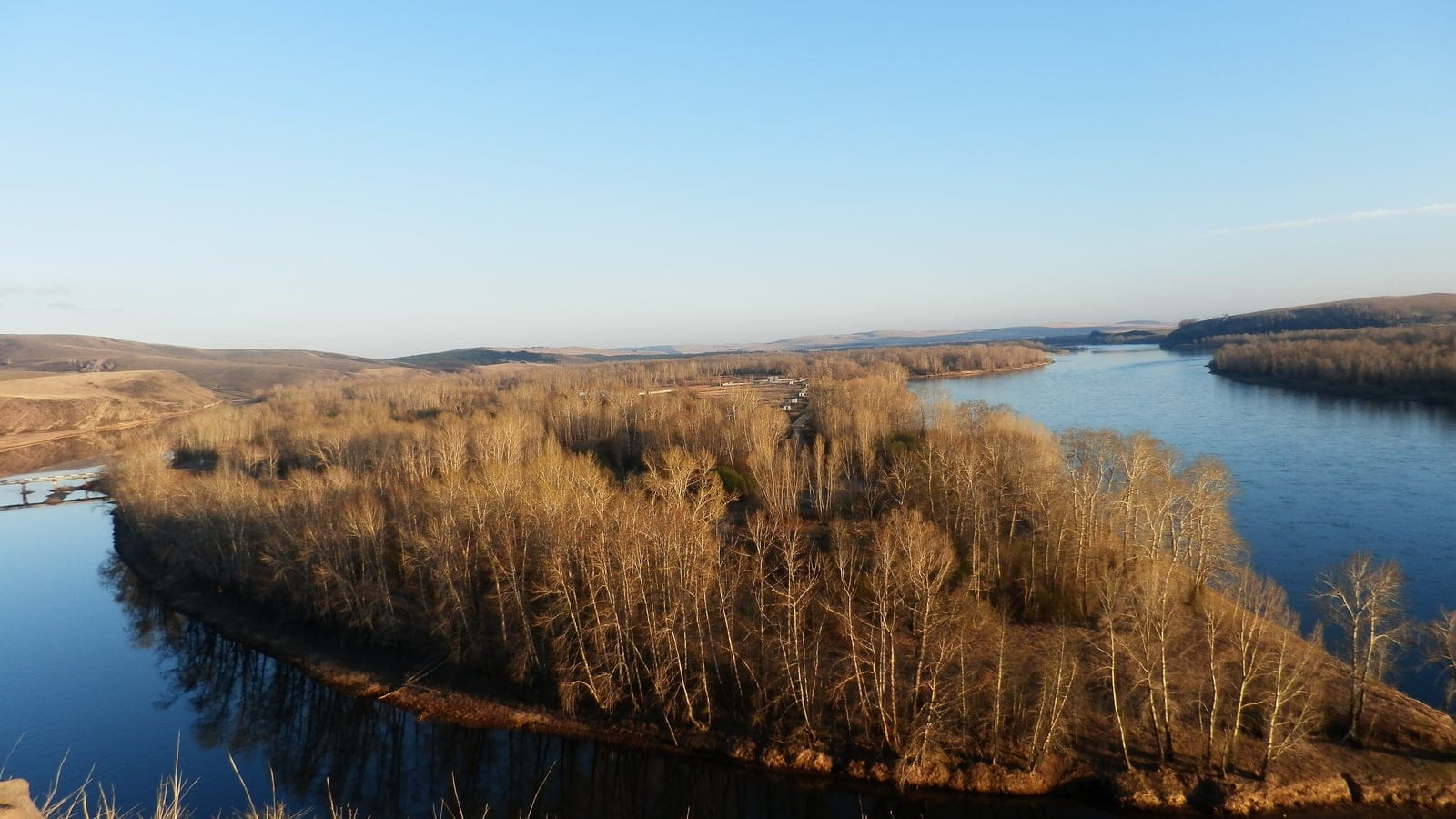 Leafless birch and poplar on a river island backed by dry steppe hills at Zelyony Bor, Krasnoyarsk Krai, Russia.