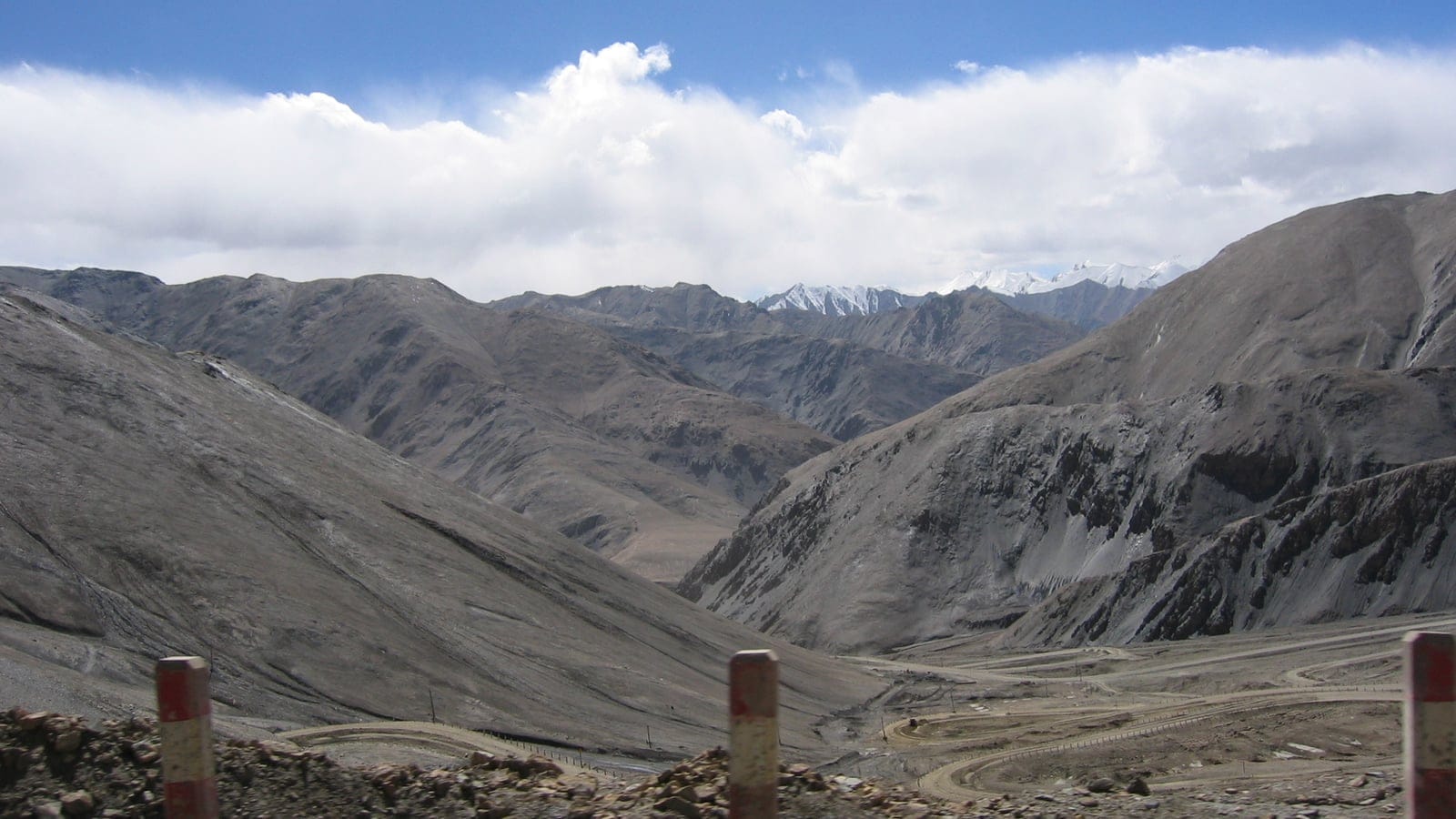 Barren grey slopes and snow peaks above a switchback road in the Kunlun Mountains.