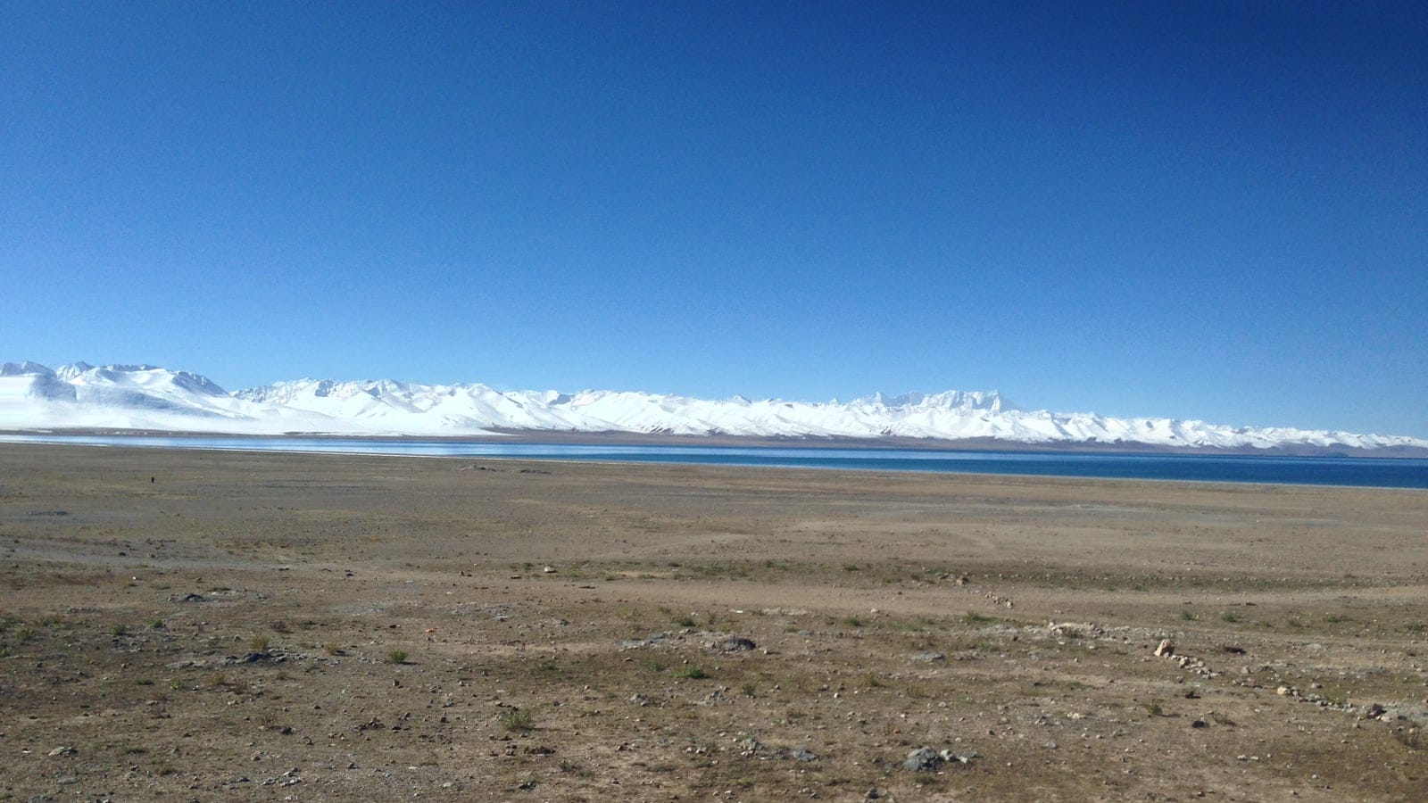 Bare gravel flat and a turquoise lake below snow-covered ranges near Damxung, Tibet.