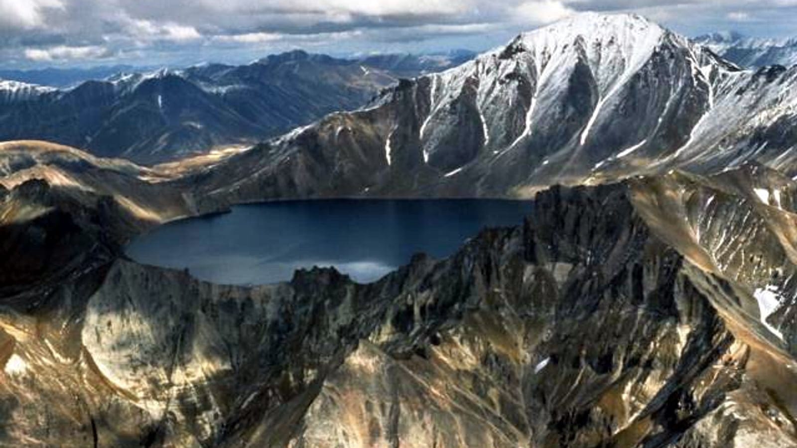 A caldera lake ringed by bare scree ridges and snow gullies at Khangar, Kamchatka, Russia.