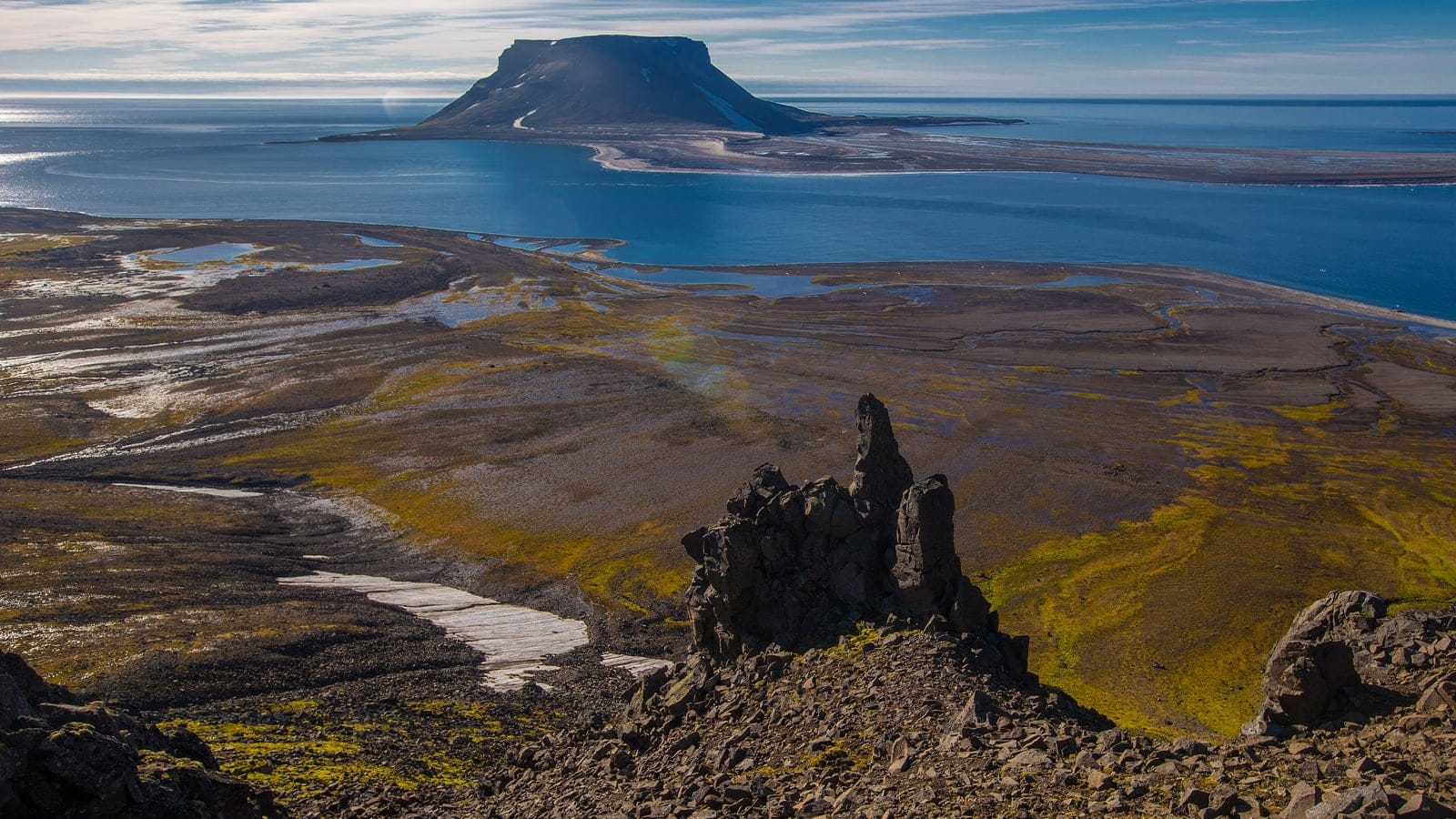 Sparse moss and lichen tundra with meltwater pools below a basalt mesa in the Russian Arctic.