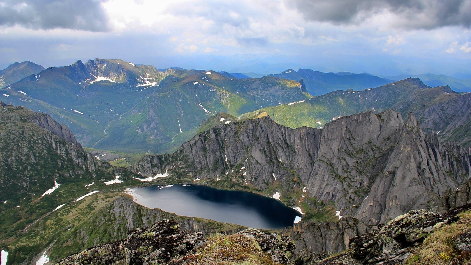 Cirque lake below granite crags with subalpine meadow and conifer patches, Trans-Baikal, Russia.