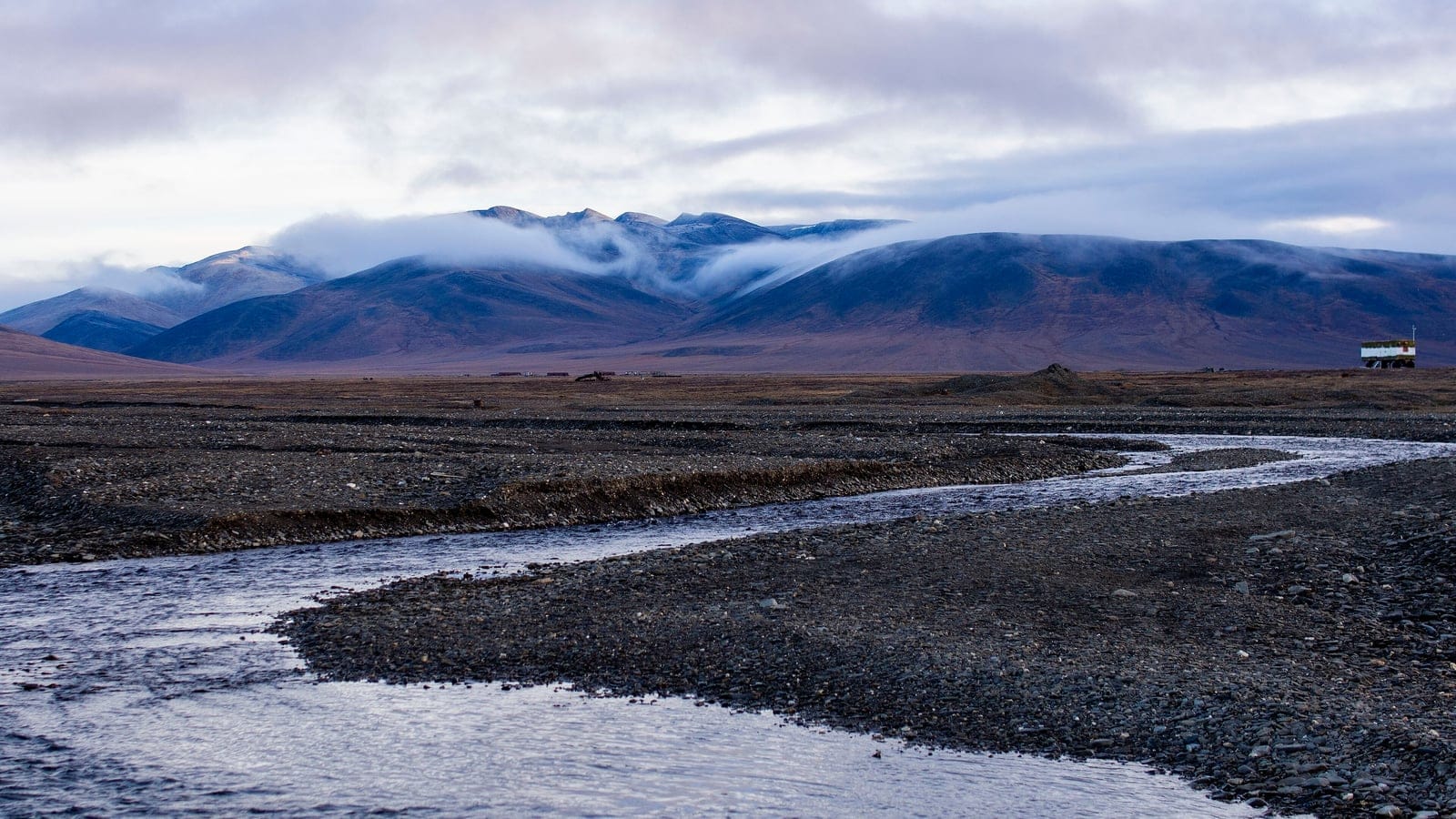 Braided gravel channels crossing bare tundra below cloud-capped hills, Somnitelnye Mountains, Wrangel Island.