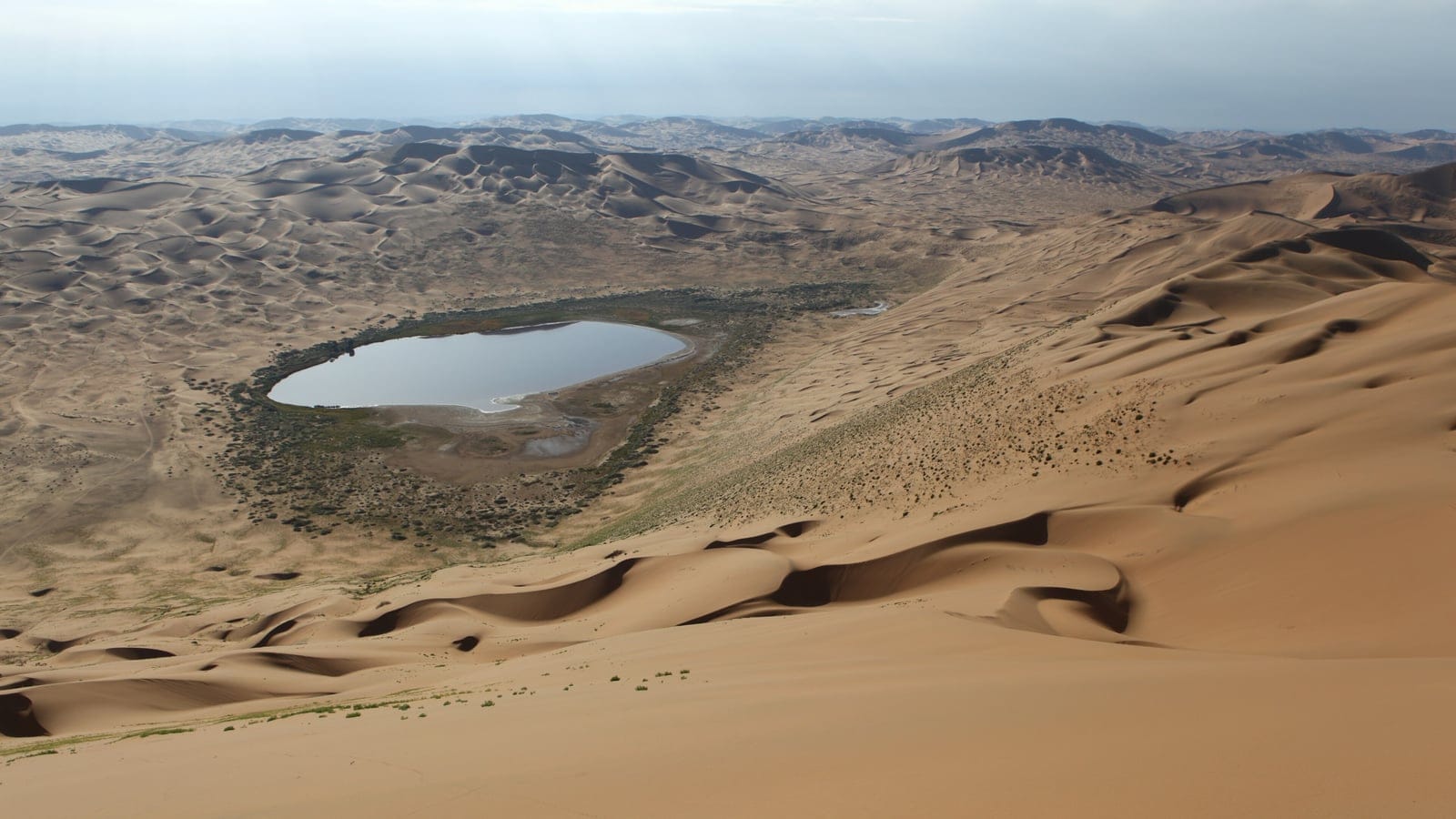 Dunes, sparse vegetation, and an interdunal lake near Bilutu Peak in the Alashan desert region.