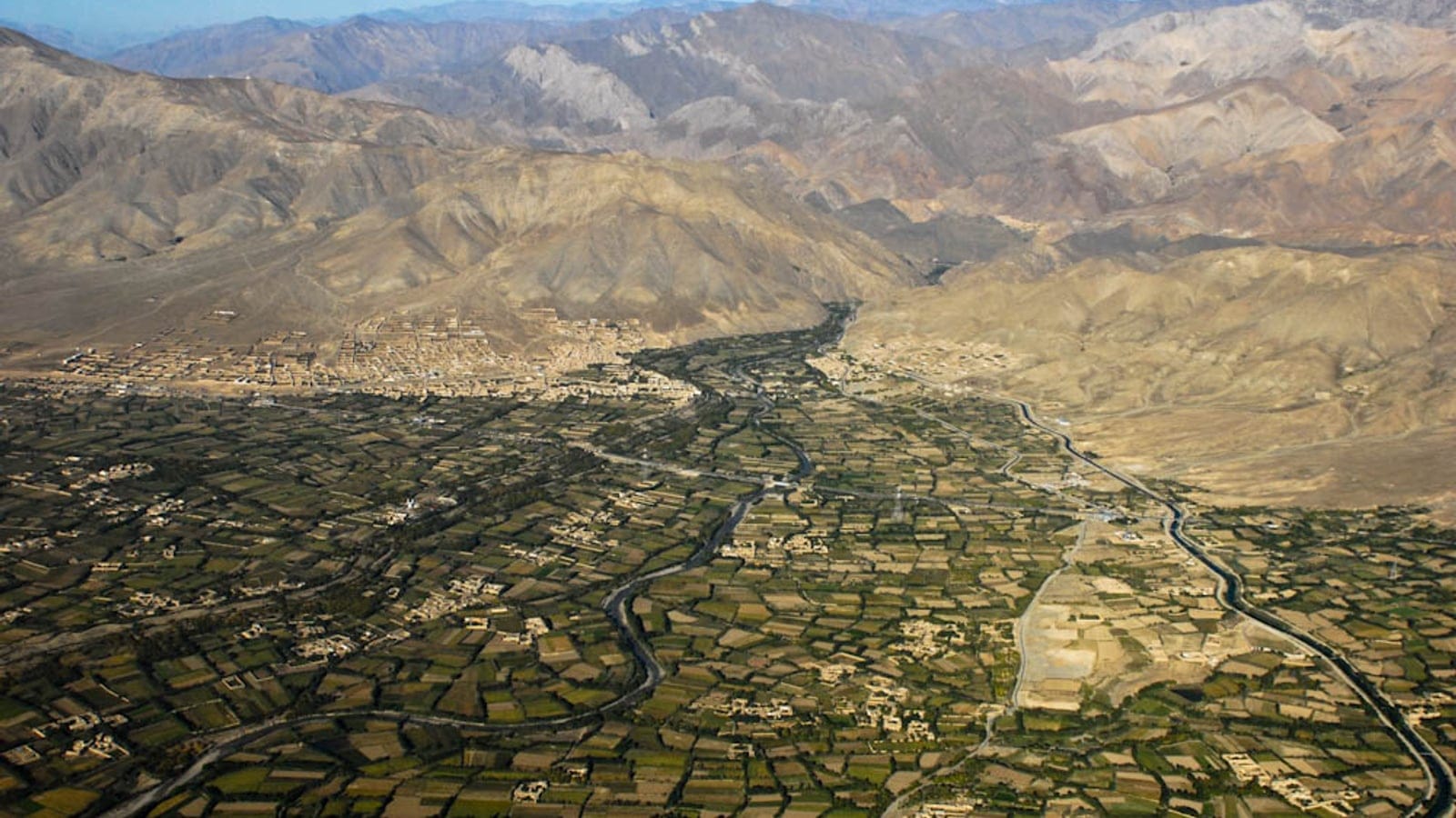 Irrigated field mosaic and compounds along a river below bare mountain slopes at Charikar, Afghanistan.