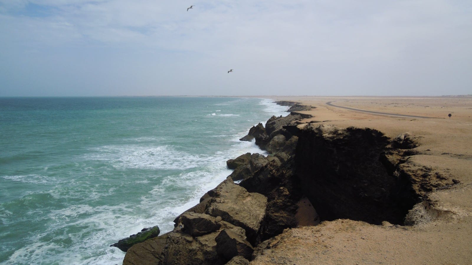 Atlantic surf undercutting low sand cliffs beside bare coastal desert near Dakhla, Western Sahara.