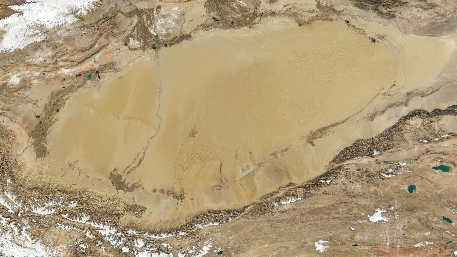 Satellite view of the Taklimakan sand sea ringed by snow-flecked mountain ranges, Xinjiang, China.