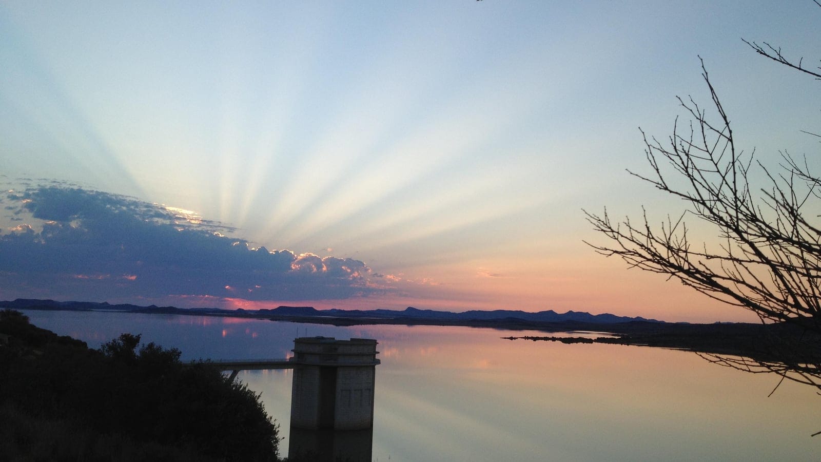 Sunrise over still water at the Gariep Dam with a concrete intake tower and leafless karoo scrub, South Africa.