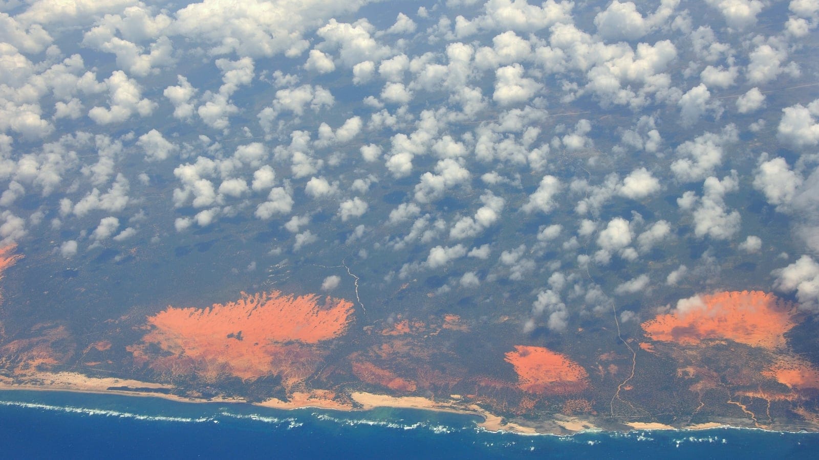 Cumulus deck over red dune sheets and the surf line of the southern Somali coast, from high altitude.